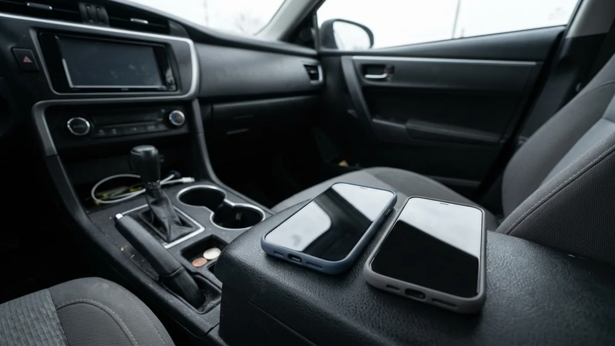 Two dark-screen phones in blue and gray cases resting beside each other on a parked car console.